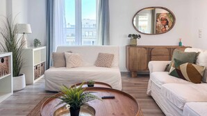 Ein modernes Wohnzimmer mit einer Couch, einem Couchtisch, einer Holzkommode und einem großen Fenster mit Vorhängen.