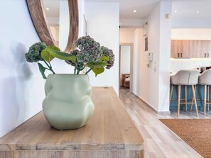 A modern interior with a wooden table, a green vase with plants, and a kitchen in the background. - Boho Flat in Glyfada Center (Glyfada)