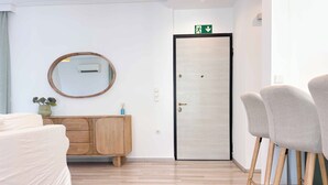 Ein modernes Hotelzimmer mit einem Holzkasten, einem runden Spiegel, einem beigen Sofa, einem braunen Teppich und einer Tür mit einem Notausgangsschild.