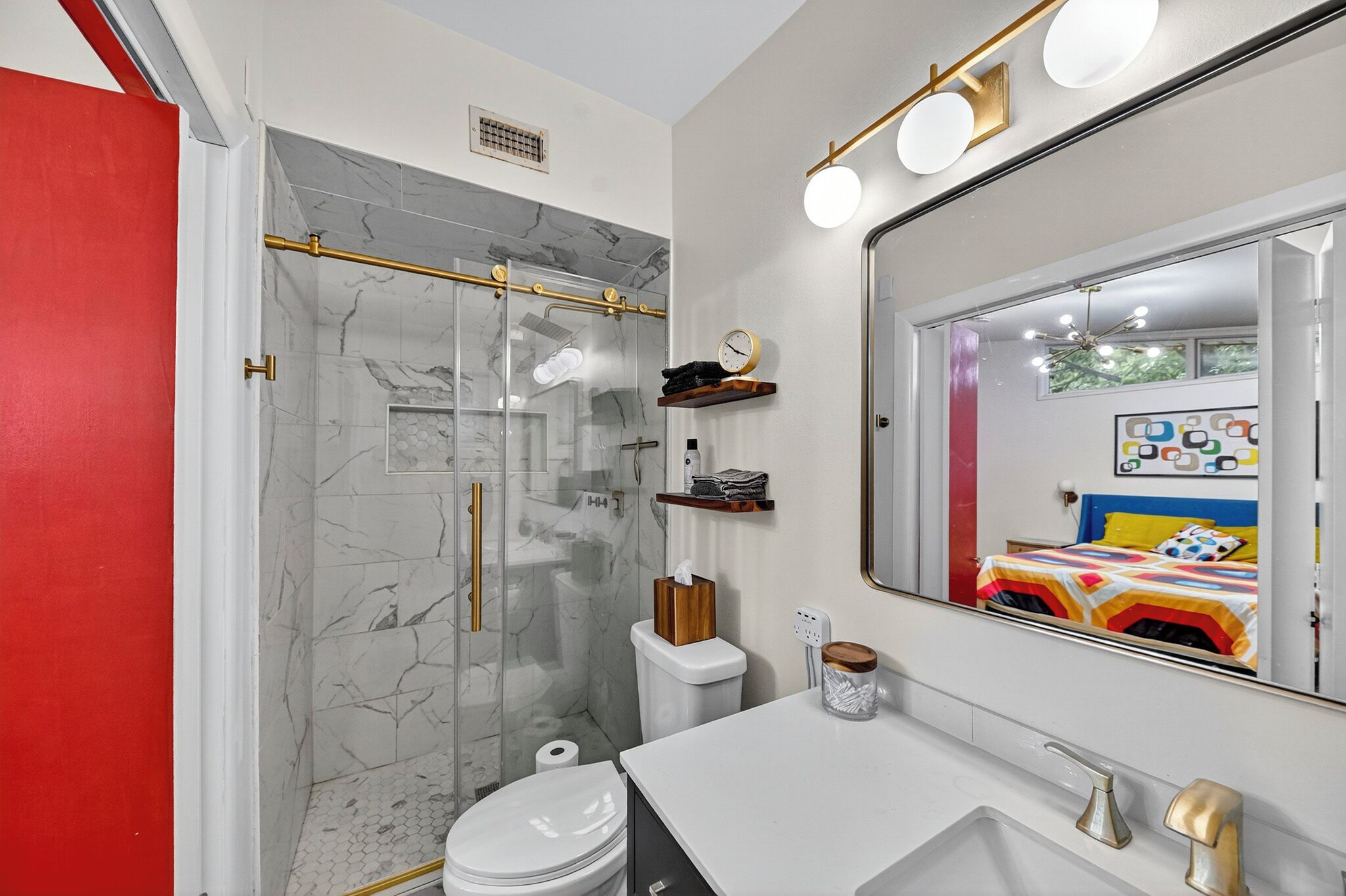Un baño moderno con ducha envuelta en vidrio, paredes de mármol, lavamanos blanco y un espejo grande con iluminación.