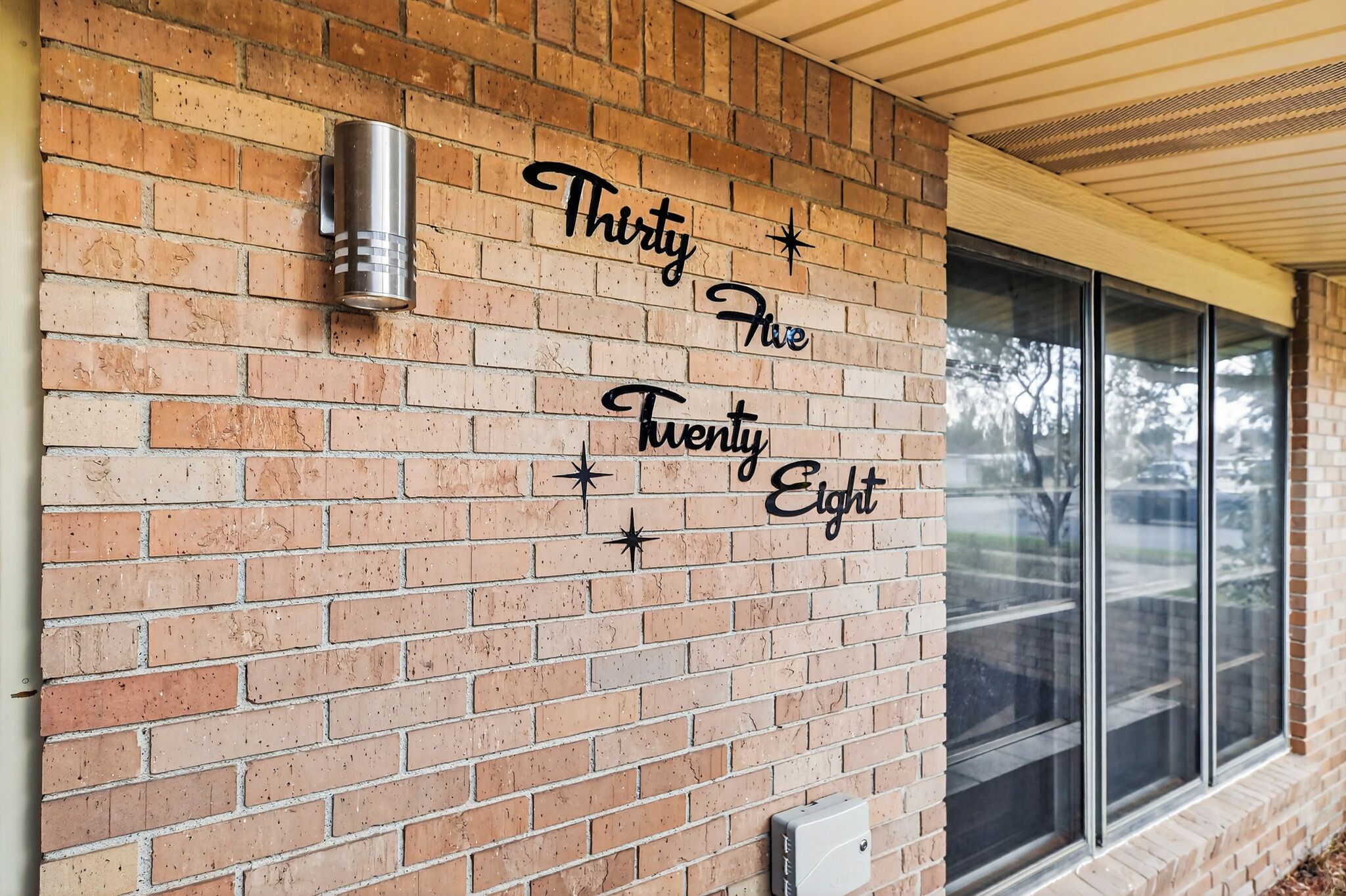 A brick wall with a decorative phrase 'Thirty Five Twenty Eight' and a metal object on the left.