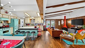 Een moderne keuken met barstoelen, een eettafel met een rode tafelkleed, en een zithoek met een bank en televisie.