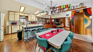 Een keuken met een eethoek, met een centraal kookeiland, barstoelen en een rode tafelkleed.