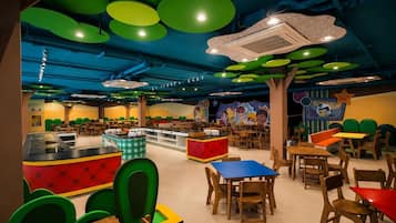 Um restaurante infantil com móveis coloridos, um balcão central e um mural na parede.