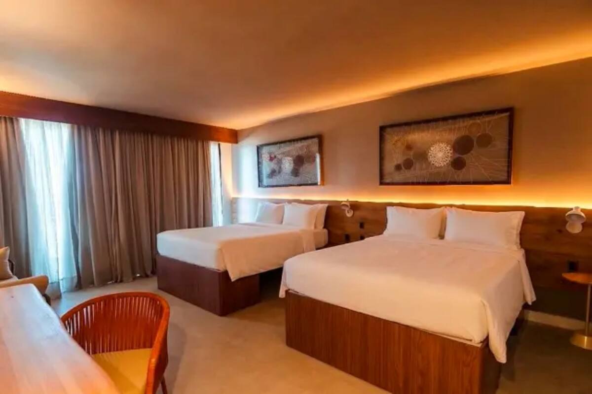 Habitación de hotel con dos camas, cabecera de madera, una mesa de comedor y una silla.