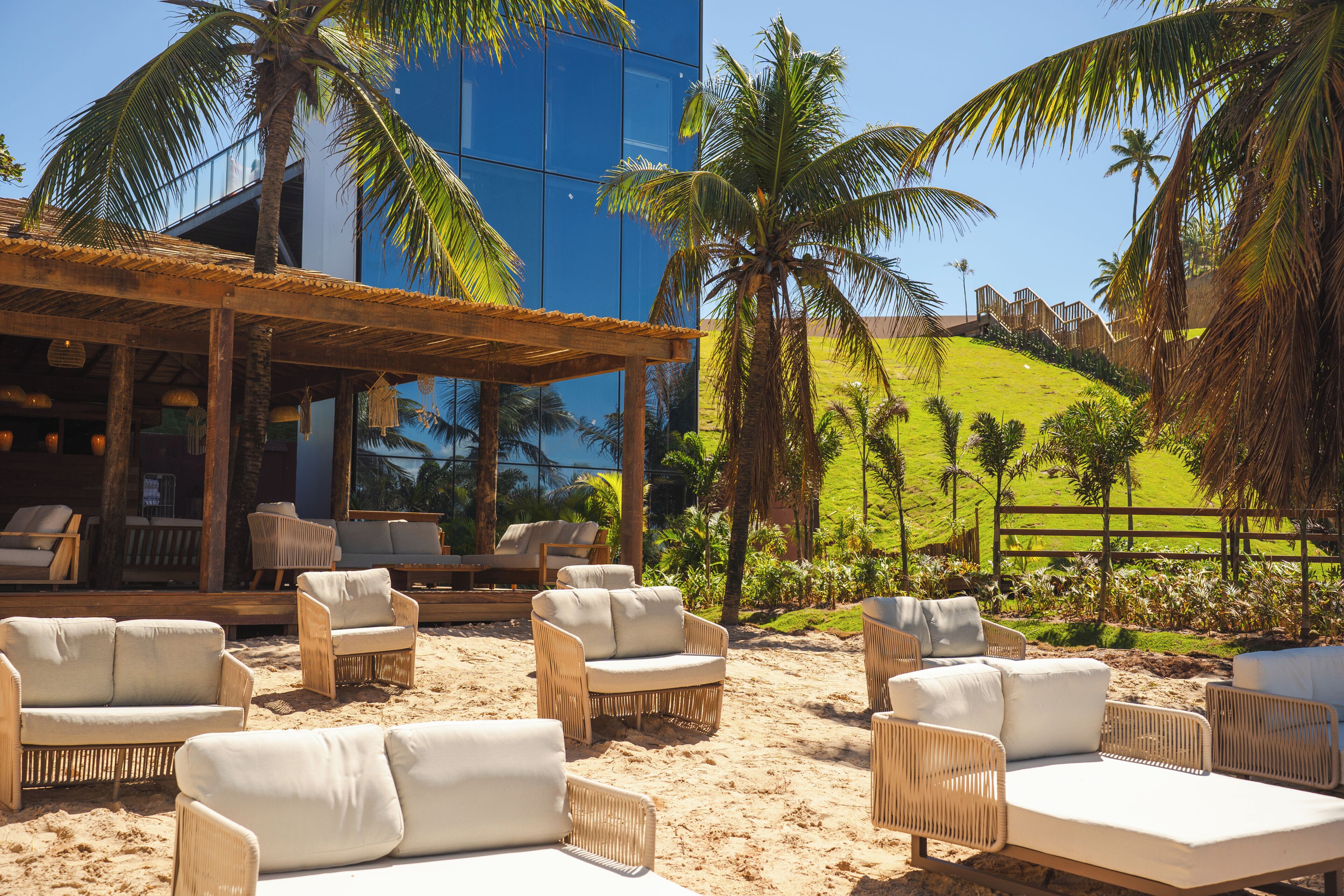A beachside lounge area with wicker furniture and a view of a blue building and palm trees.
