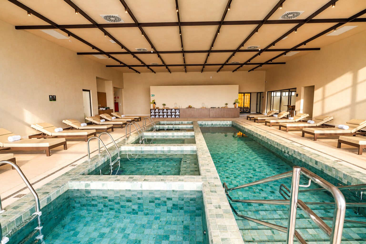 Una amplia piscina cubierta con varias pistas, tumbonas y suelo de baldosas.