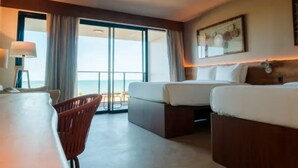Habitación de hotel con dos camas, un escritorio, una silla y un ventanal con vistas.