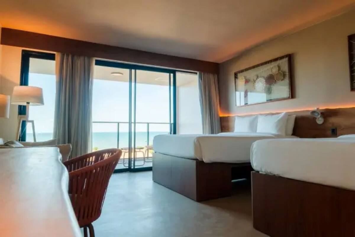 Habitación de hotel con dos camas, un escritorio, una silla y un ventanal con vistas.