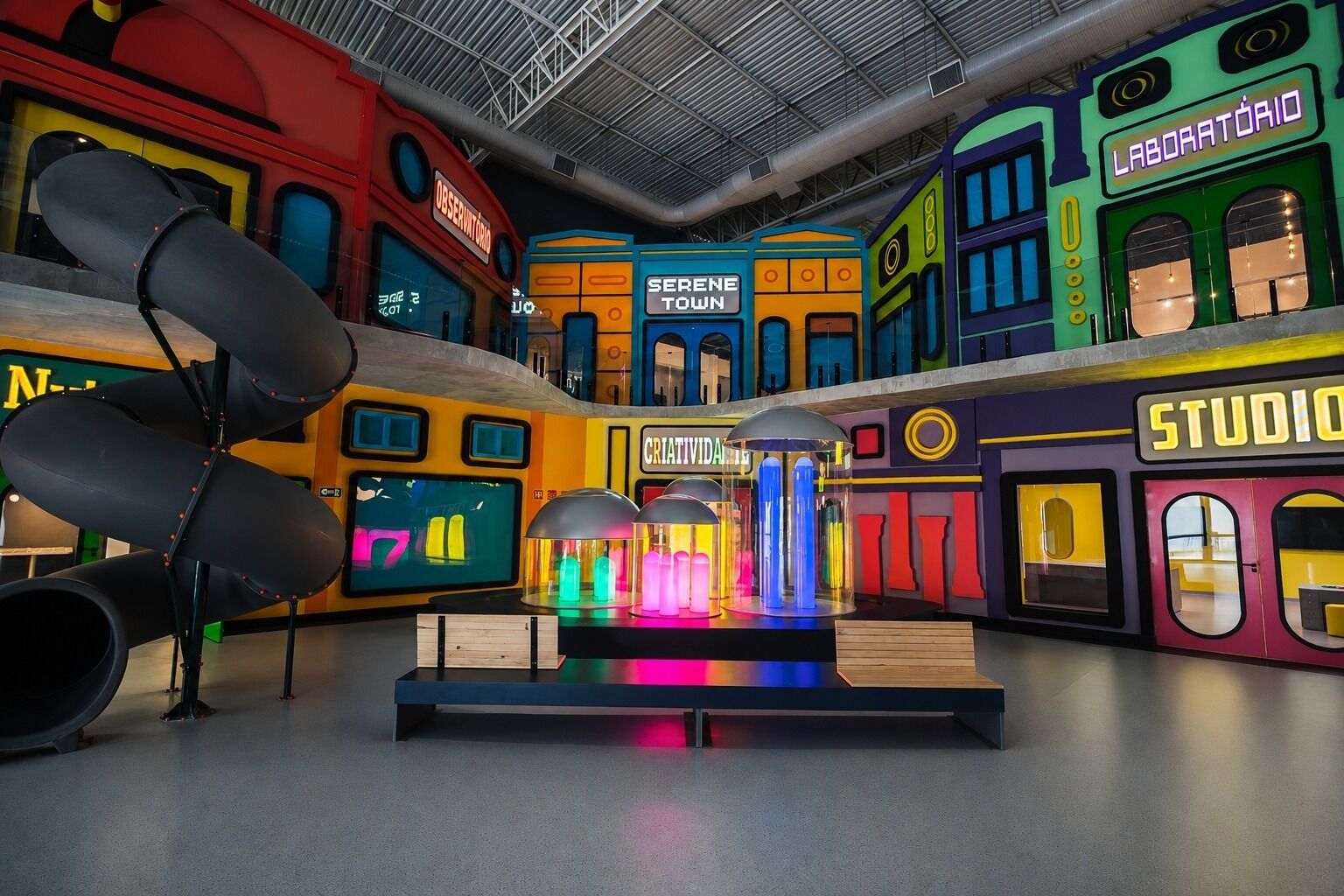 Um espaço interior colorido com várias áreas identificadas, como 'LABORATOIO', 'STUDIO' e 'SERENE TOWN'.