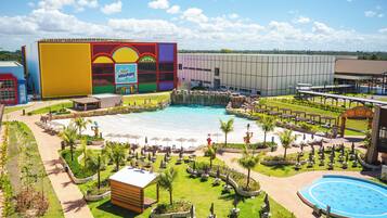 Resort com uma piscina grande, áreas de estar ao ar livre e um edifício colorido com design de sol e ondas.