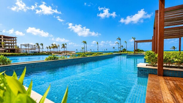Una piscina con agua azul cristalina, rodeada de vegetación y una terraza de madera.