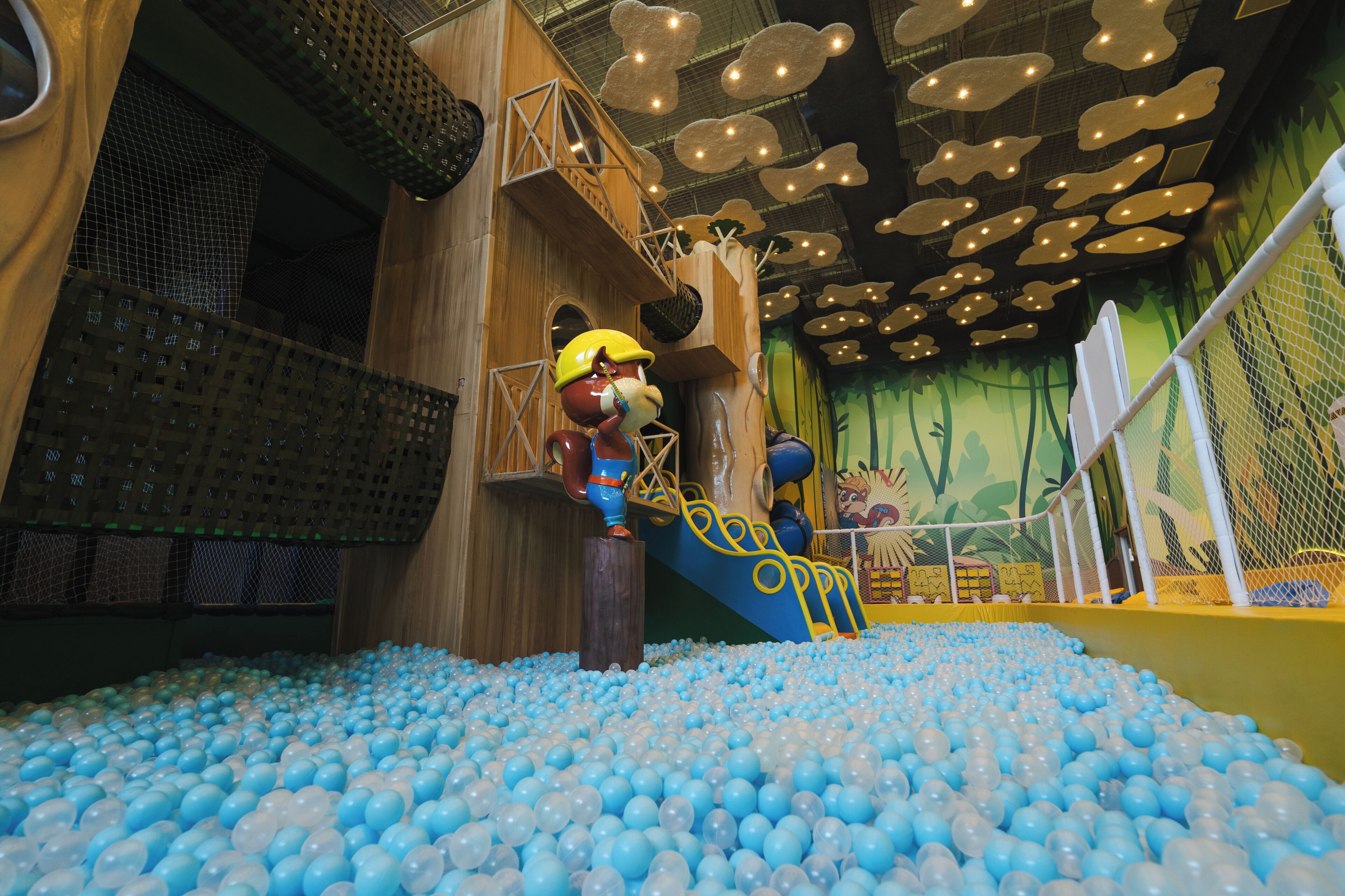 Espaço de brincadeiras com piscina de bolinhas, estruturas de escalada e paredes com rede.