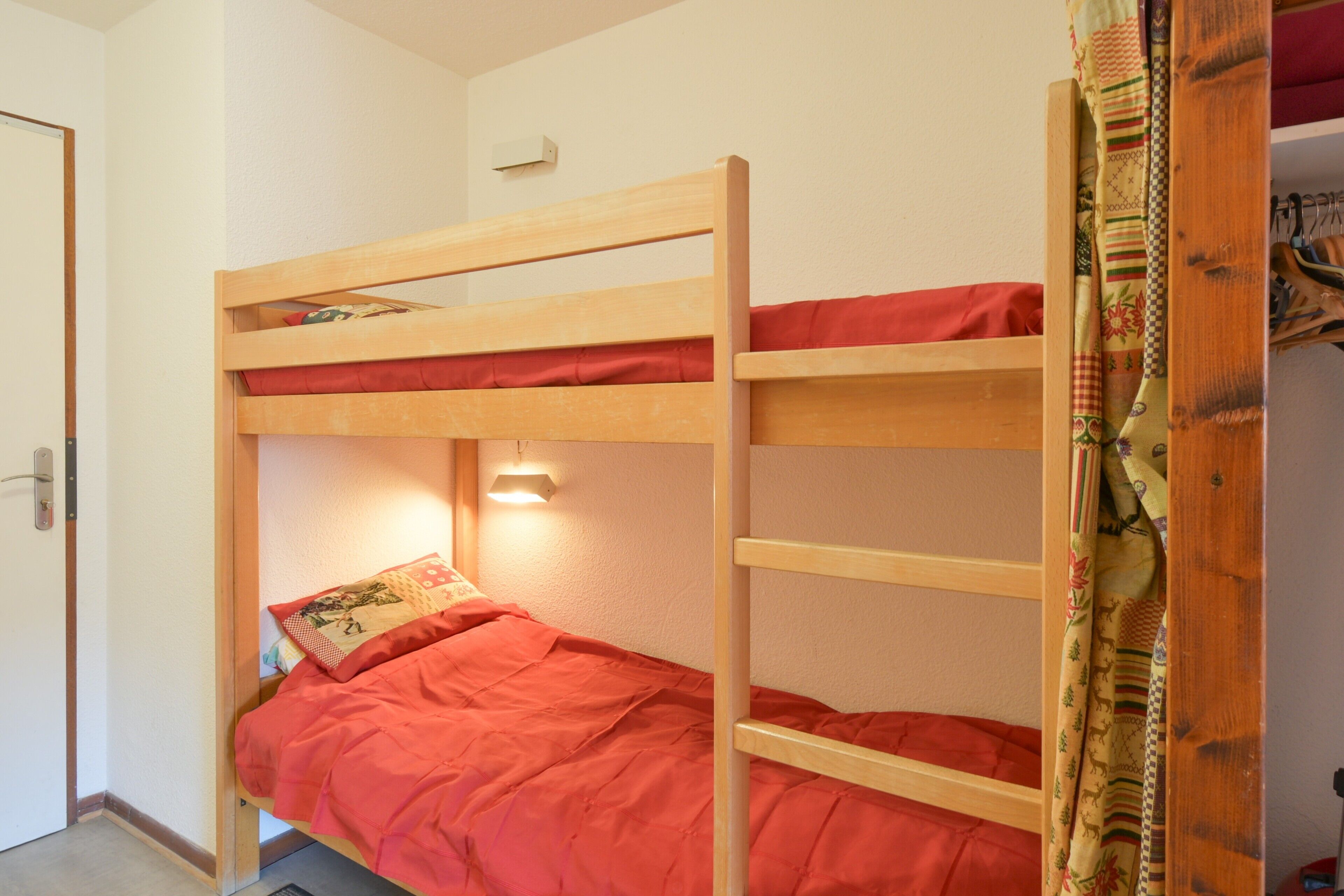 Un lit superposé avec un matelas rouge, une échelle en bois et une lampe fixée au mur.