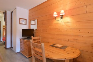 Una habitación con paneles de madera, un televisor sobre un mueble de madera, una mesa con camino de mesa y una lámpara fijada a la pared.