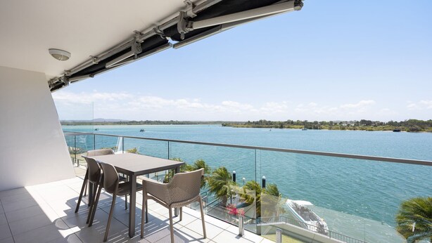 A balcony with a table and chairs overlooking a large body of water, with a view of the coastline and boats. - Commodore 6 Noosa Heads (Noosa Heads)