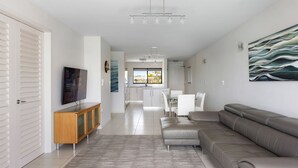 A modern living room with a sofa, TV, wooden cabinet, and a kitchen in the background. - Commodore 6 Noosa Heads (Noosa Heads)