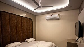 A modern hotel room with a bed, a ceiling fan, an air conditioning unit, a television, and a marble-patterned floor. - Hotel Kapil Royal Inn (Haridwar)