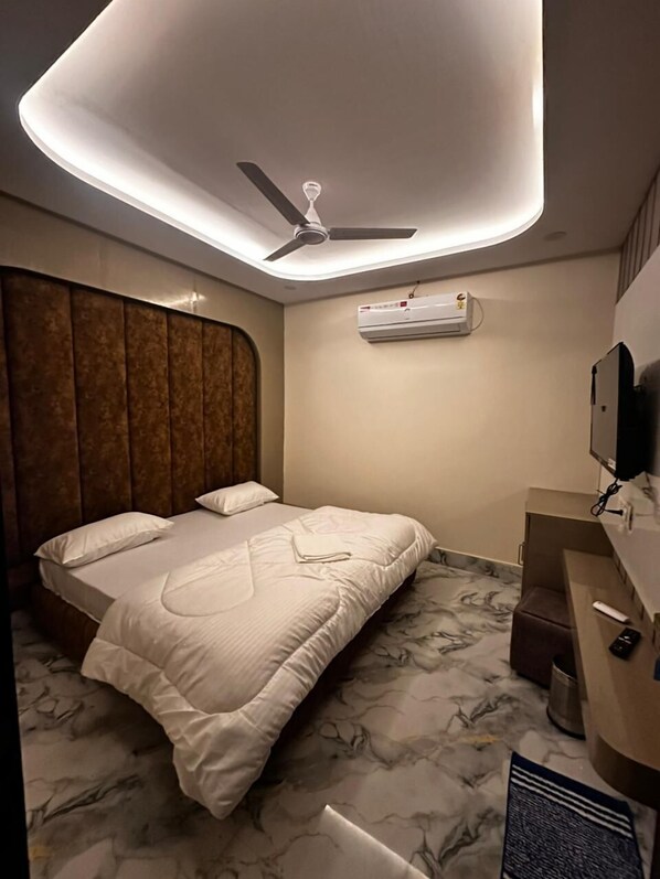A modern hotel room with a bed, a ceiling fan, an air conditioning unit, a television, and a marble-patterned floor. - Hotel Kapil Royal Inn (Haridwar)