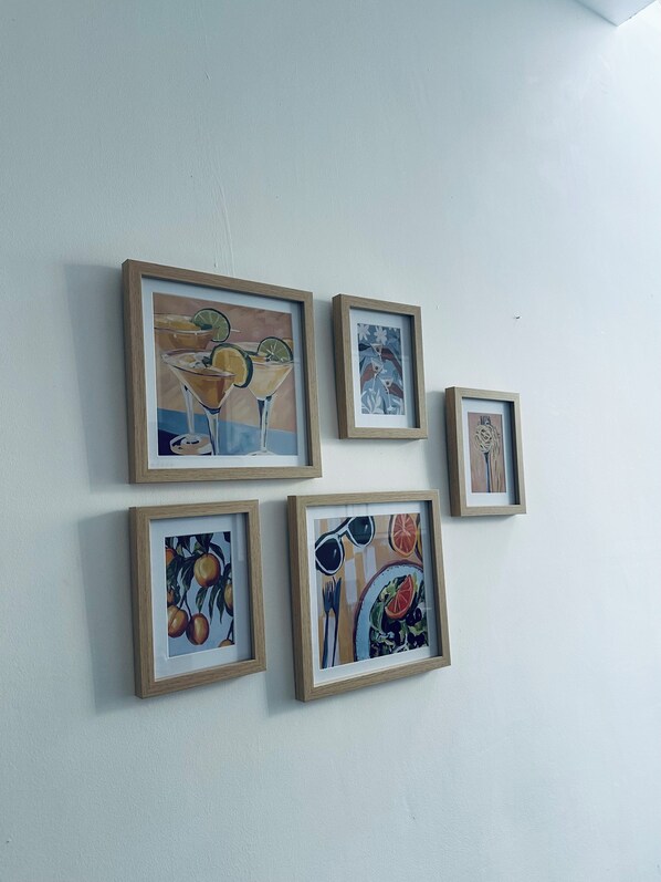 Five framed artworks on a plain wall.