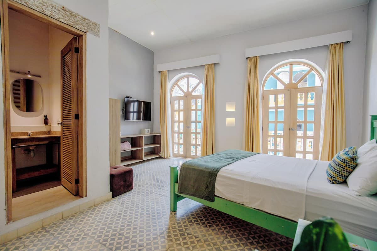 Une chambre à coucher avec un lit, une télévision, une armoire et une fenêtre avec des rideaux.