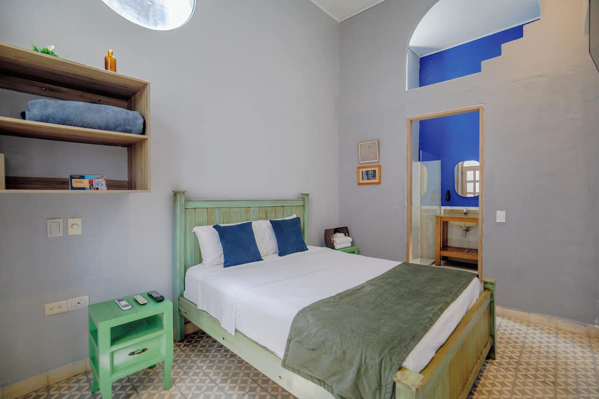 Une chambre à coucher avec un lit, une table de chevet, une étagère avec des serviettes, un miroir et un sol à motifs.