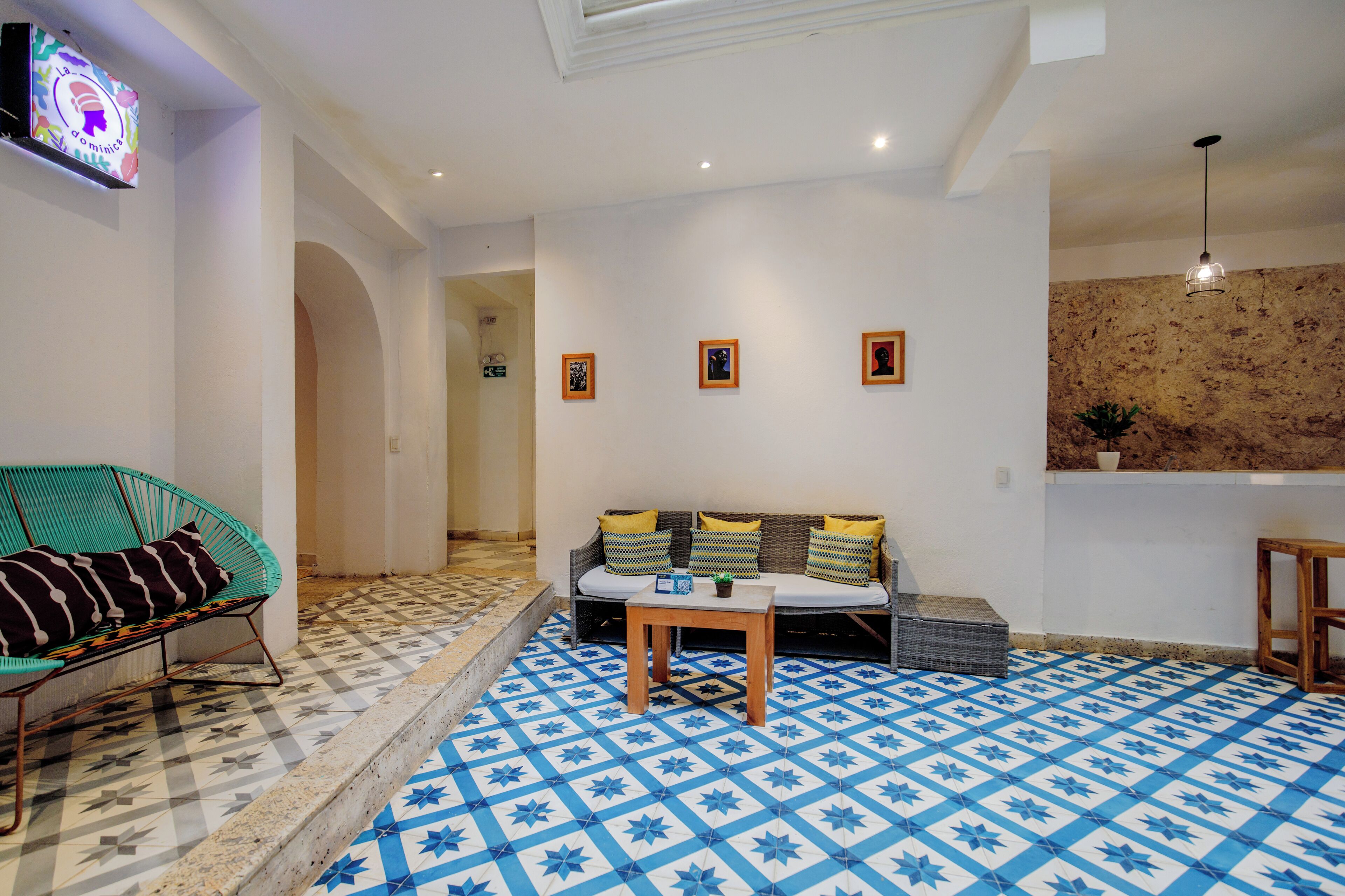 A room with a patterned floor, a sofa with cushions, a small table, and a television mounted on the wall.
