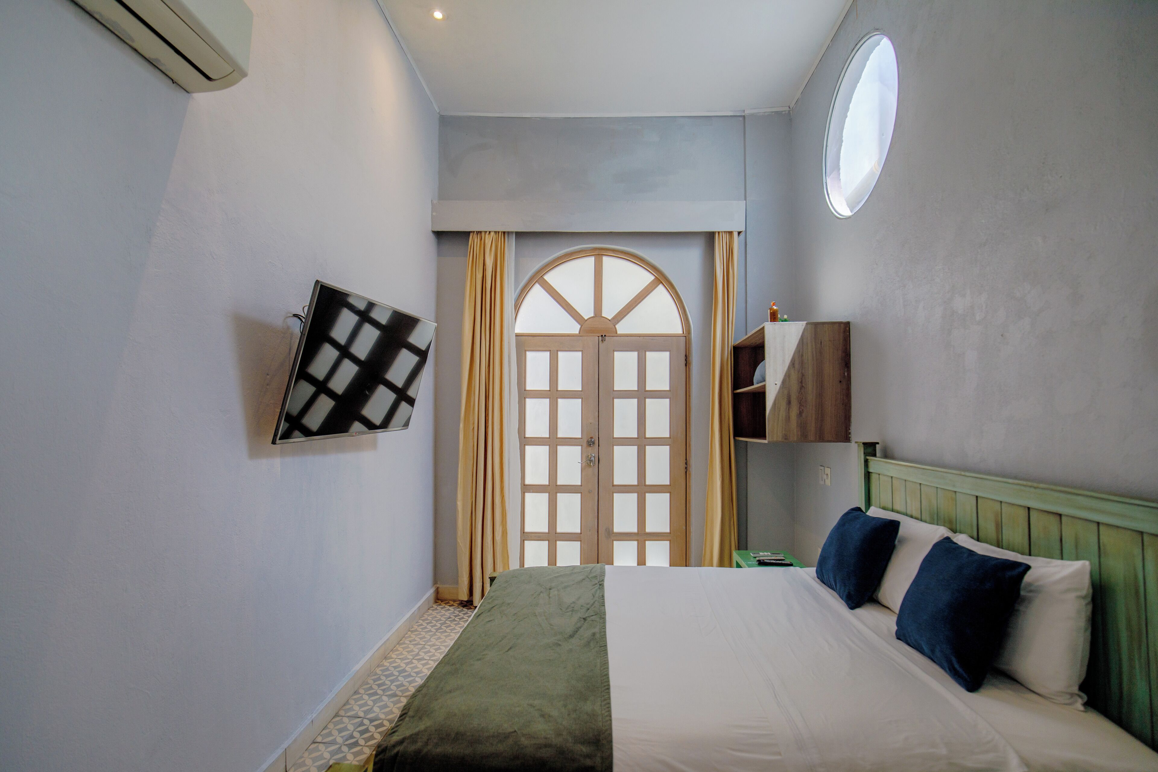 A bedroom with a bed, a window, a door, and a wall-mounted air conditioner.