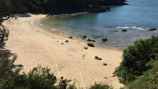 En strand med klart vatten, sandstrand och klippiga utskjutande partier.