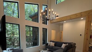 Un salon moderne avec de grandes fenêtres, un lustre et un canapé gris.