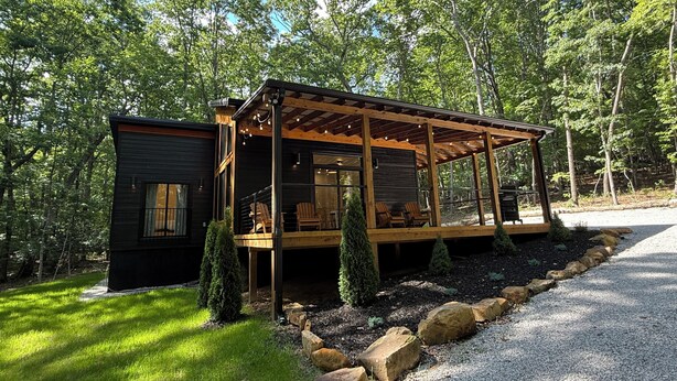 Une cabane dotée d’un porche couvert, d’une petite terrasse et d’une allée gravillonnée.