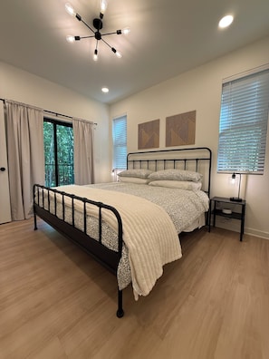 A bedroom with a bed, a bedside table, a wall-mounted light fixture, and a window with blinds. - Creekside Nook in Sewanee (Sewanee)