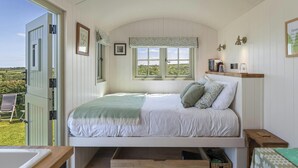 A bedroom with a bed, a window, a shelf with books, and a view of the outdoors.