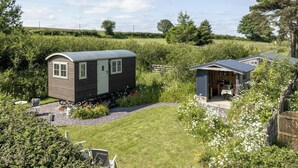 A small, single-story house with a curved roof, surrounded by a well-maintained garden and a grassy field.