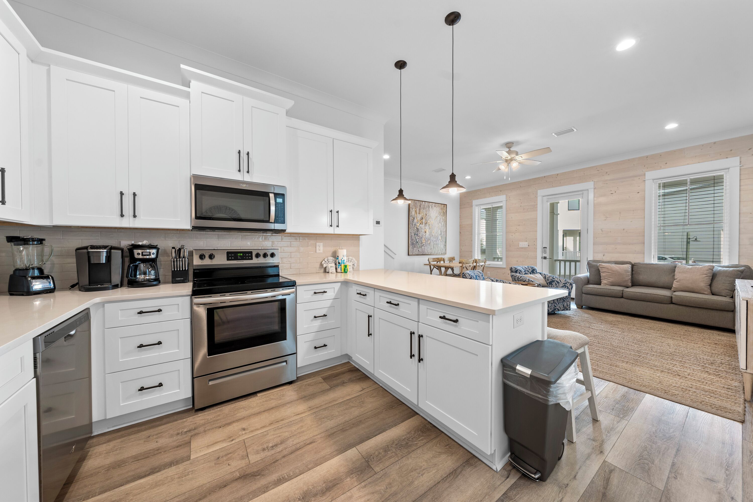 A modern kitchen with white cabinets, stainless steel appliances, and a wooden floor.