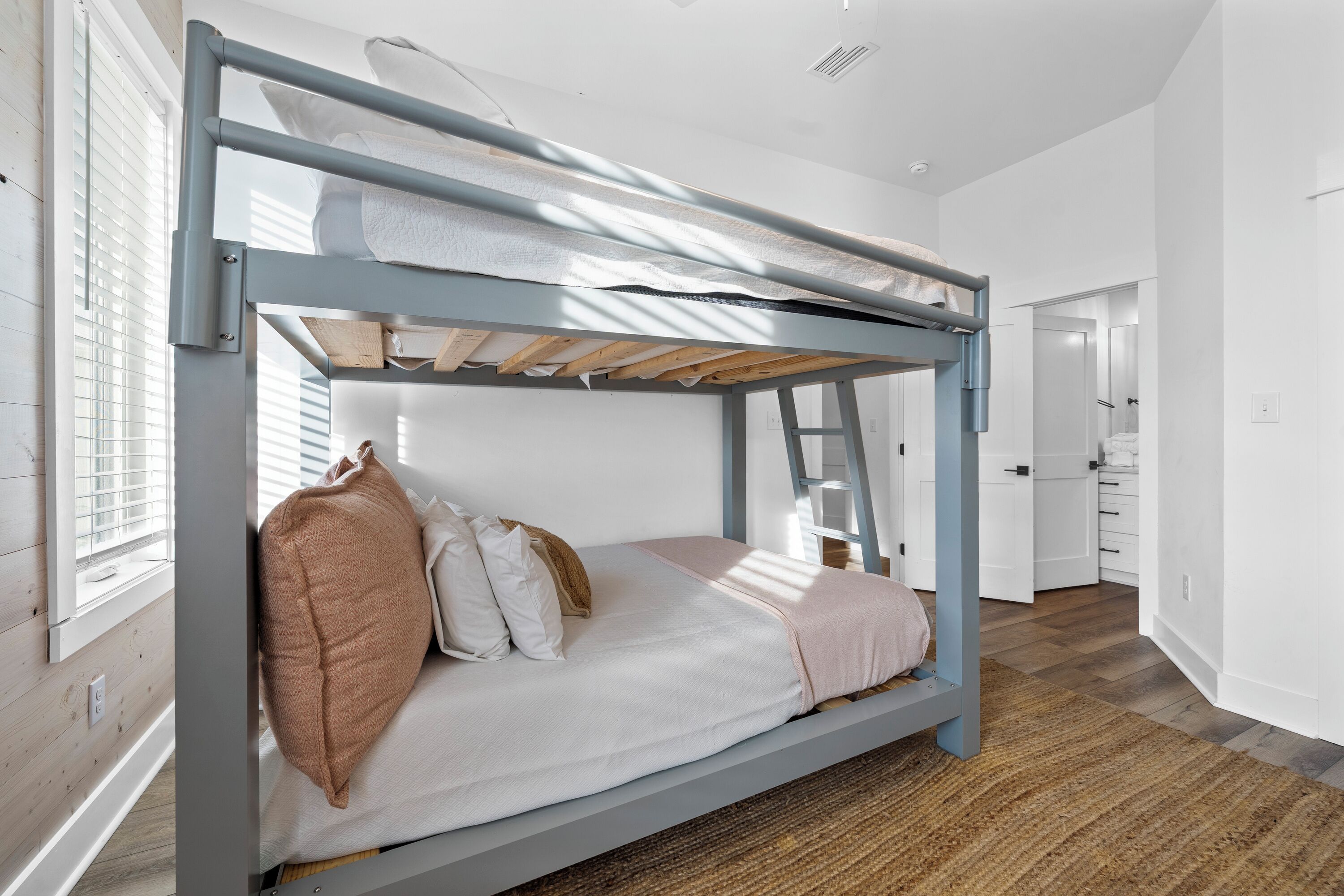 Ein Stockbett mit Holzleiter, weißer Bettwäsche und einem gewebten Teppich auf dem Boden.