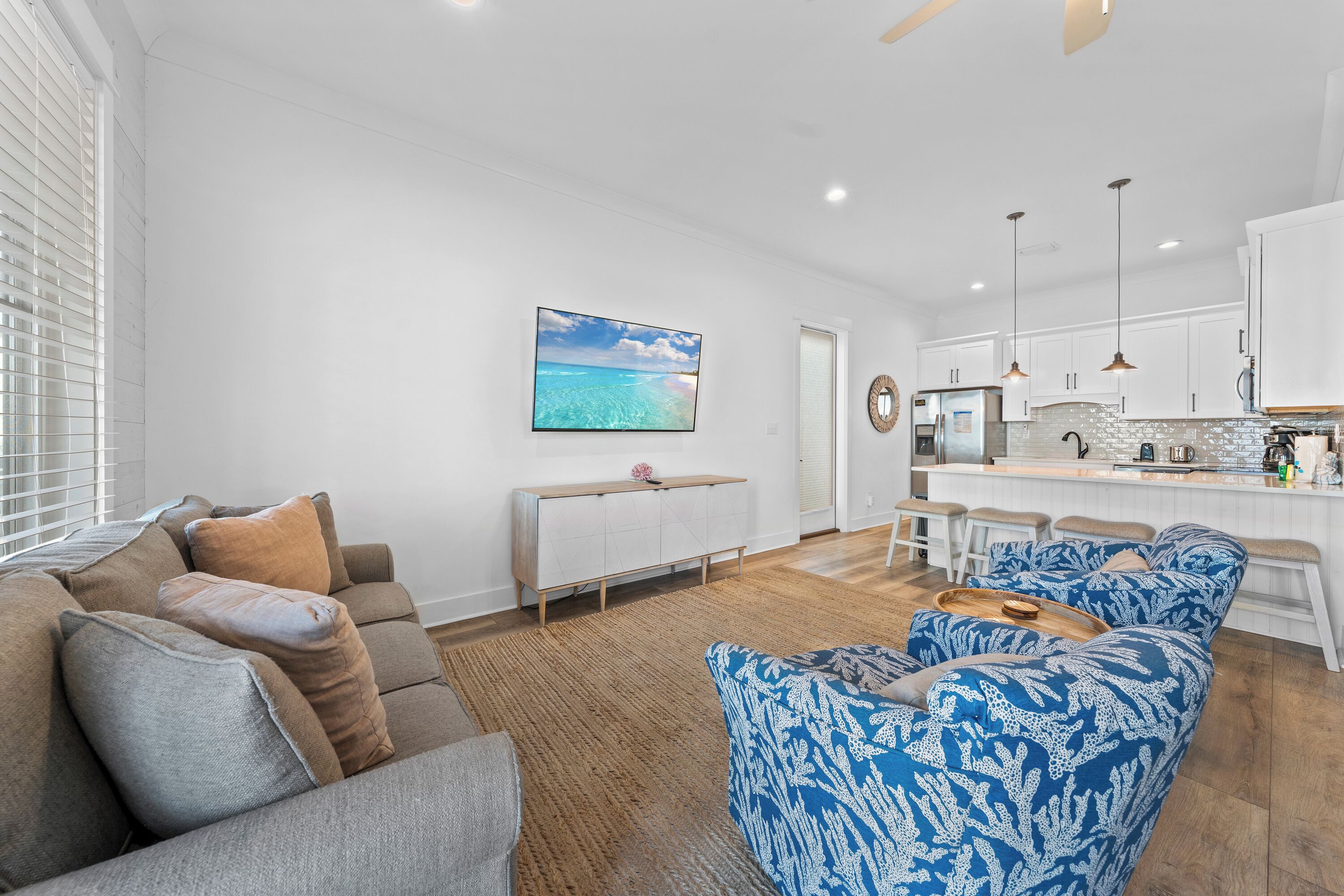 A modern living room with a sofa, a patterned armchair, and a coffee table. There is a kitchen area with a bar and white cabinets.