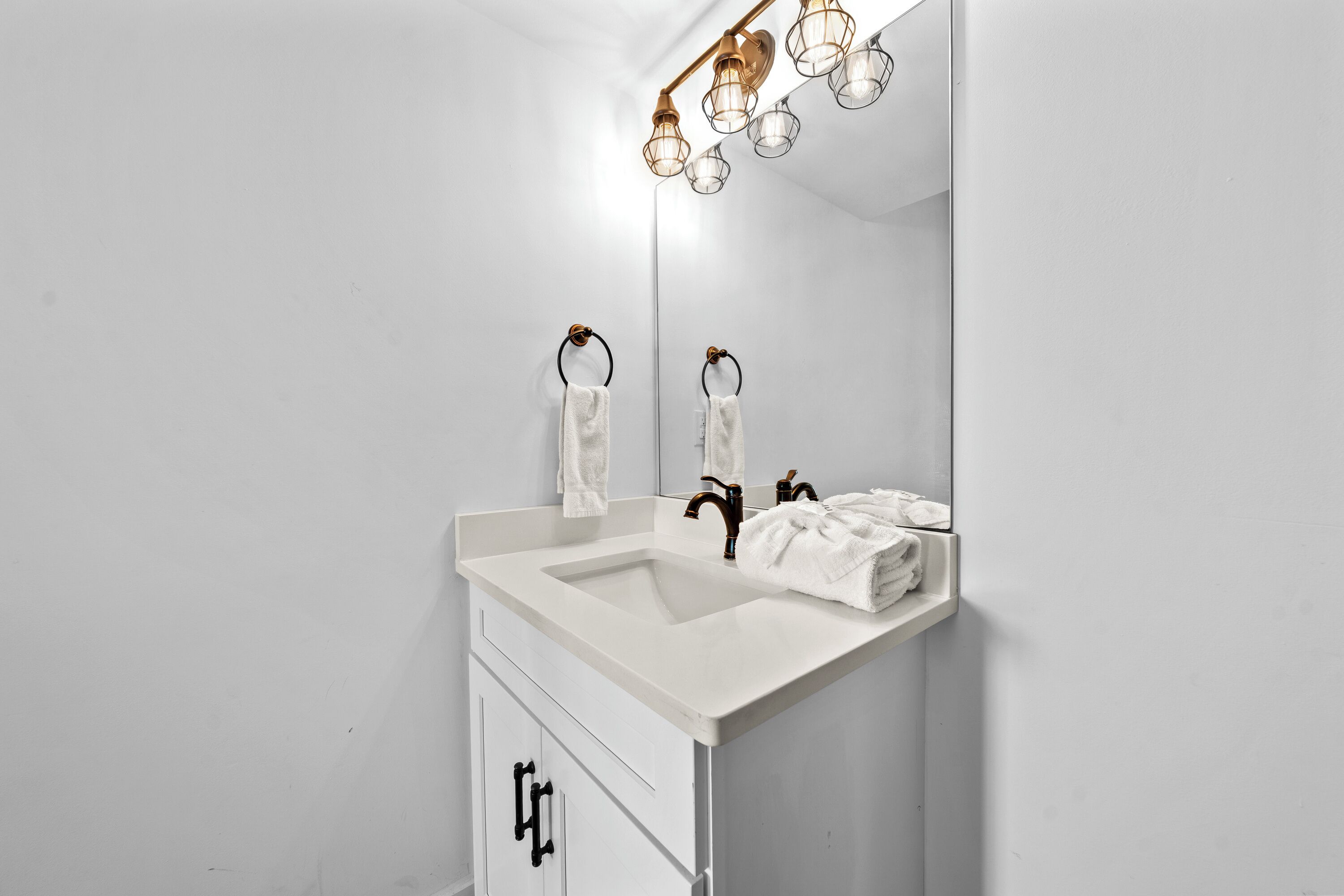 A modern bathroom with a white sink, two towel rings, and a mirror with a light fixture above.