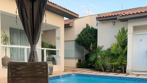 A poolside area with wicker furniture, a table with two glasses and a tray of grapes, and a view of the pool and surrounding greenery. - Prosper Executive Hotel (Capivari)