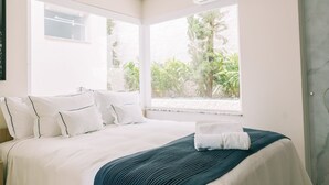 A neatly made bed with white bedding and a teal throw blanket, a window with a view of greenery, and a marble wall. - Prosper Executive Hotel (Capivari)