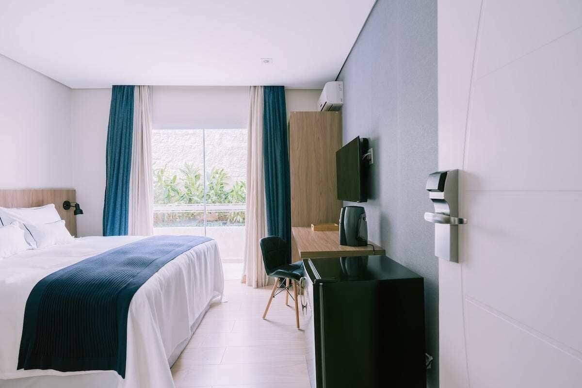 A hotel room with a bed, a desk, a chair, a TV, and a window with curtains.