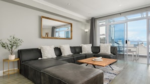A modern living room with a sectional sofa, a wooden coffee table, and a large window offering a view of the outdoors.