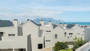 A residential area with modern buildings, a clear sky, and a distant view of the sea and mountains.