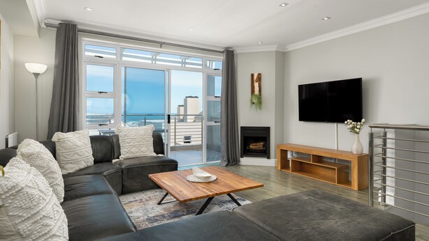 A modern living room with a sectional sofa, a wooden coffee table, and a flat-screen TV mounted on the wall.