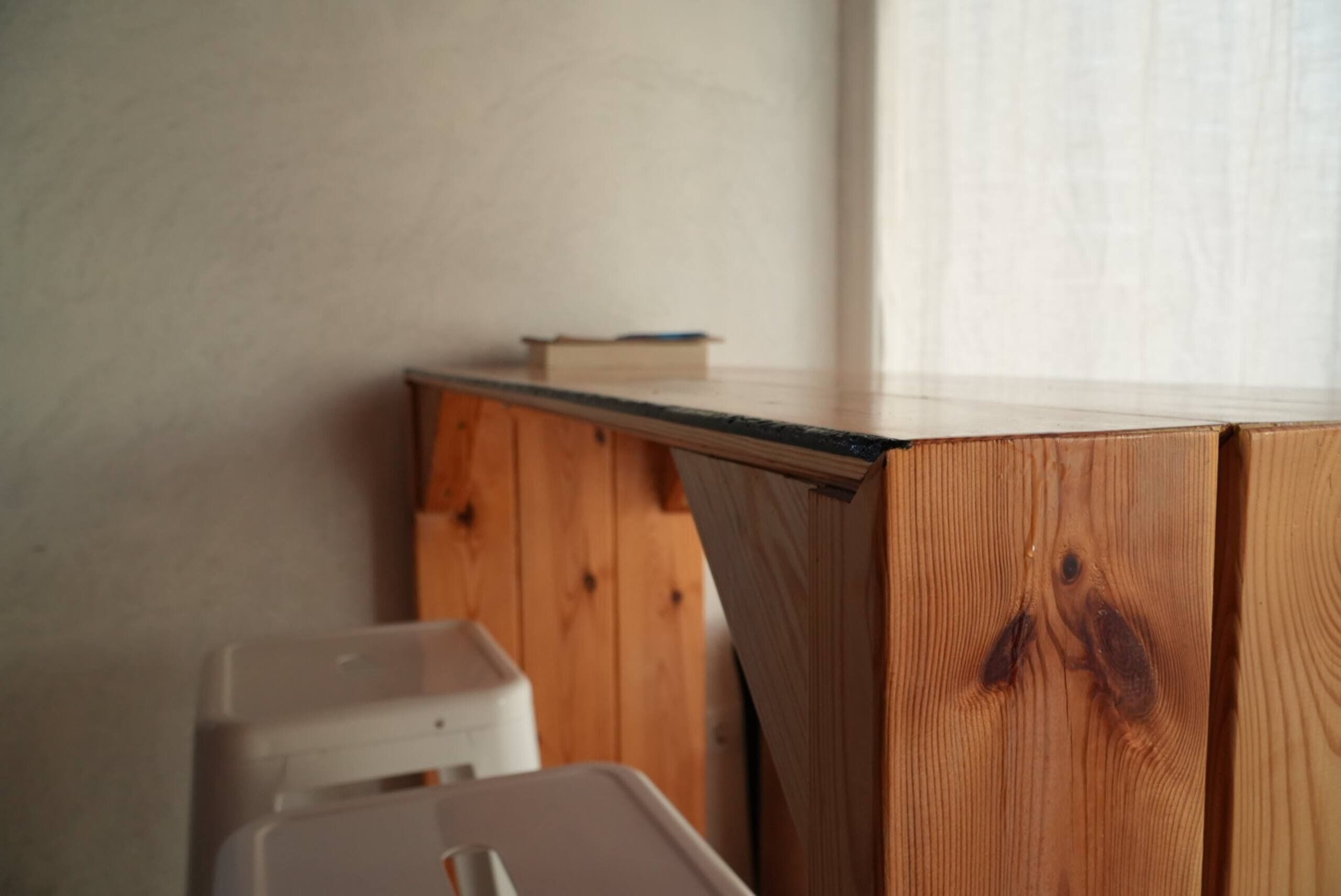 Una esquina de una habitación con un escritorio de madera y un cubo de basura blanco.