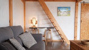 A cozy living room with a gray sofa, a wooden ladder, a small table with chairs, and a painting on the wall. - Cozy Private Duplex in Vitamin Sea Guestouse in Lajares (La Oliva)
