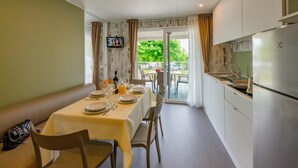 A dining area with a table set for four, a sofa, and a kitchen with a refrigerator and sink. - Vacation village Le Palme Mobilehome Lodge Comfort for 5 persons (Pacengo di Lazise)