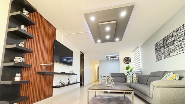 A modern living room with a flat-screen TV, built-in shelves, a grey sofa, and a coffee table. - Relaxing House just 5 minutes form the San Juan Airport (Carolina)