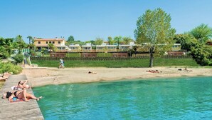 A pool area with a wooden deck, clear blue water, and a row of villas in the background. - Vacation village Le Palme Mobilehome Lodge for 4 people (Pacengo di Lazise)