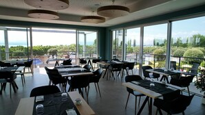 A modern dining area with tables and chairs, large windows offering a view of the outdoors. - Vacation village Le Palme Mobilehome Lodge for 4 people (Pacengo di Lazise)